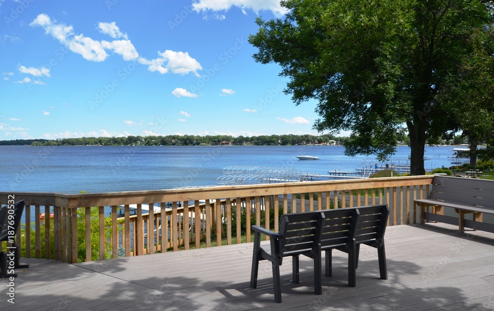 Patio deck with chairs and bench overlooking the lake on a sunny summer day