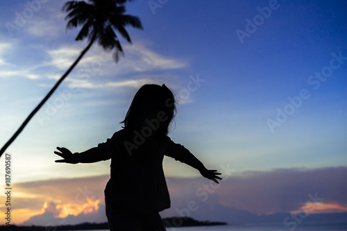 silhouette little girl flying and rising hands on sunset blue sky on the beach.Vintage tone filter effect color style.Freedom and feel good concept.