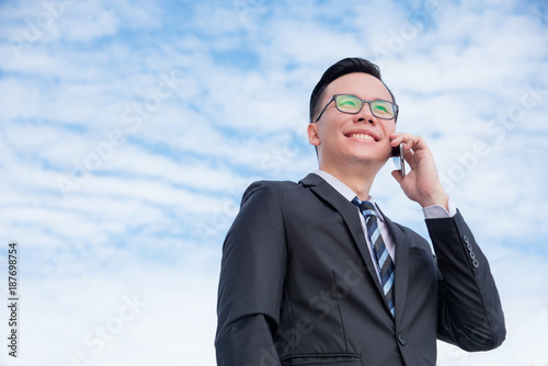Young asian businessman in black suit talking with someone via smart phone