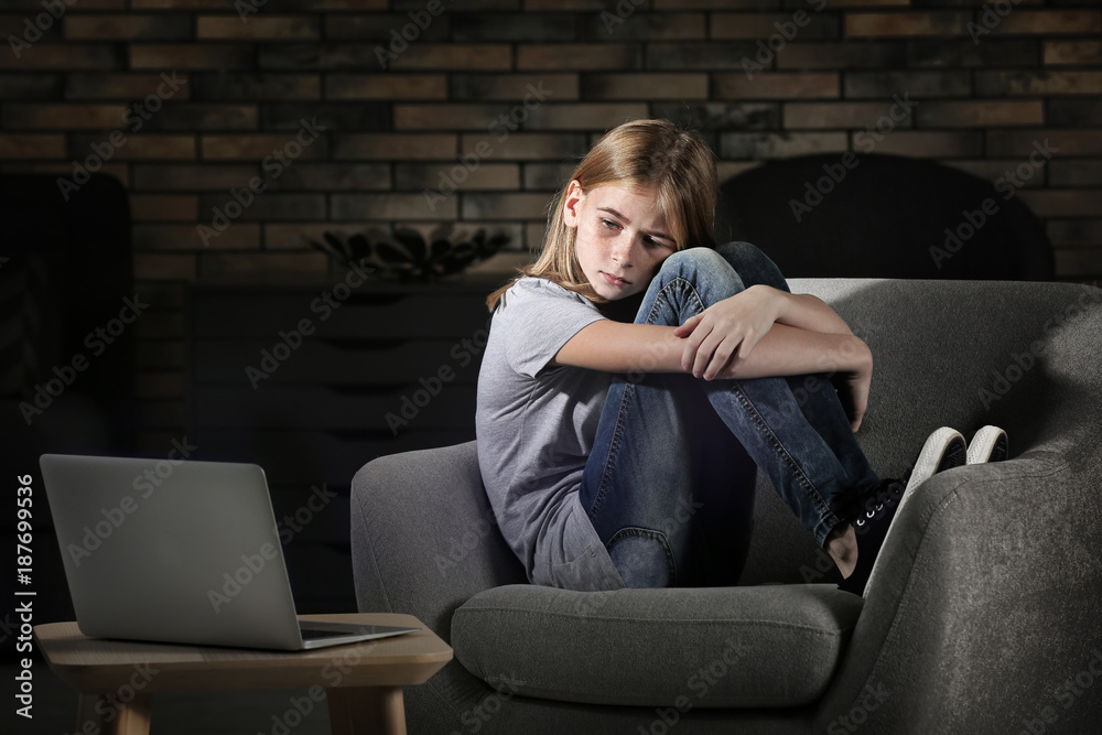 Sad teenage girl sitting near laptop in dark room