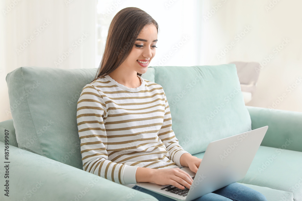 Young woman with modern laptop sitting on sofa at home Young woman with modern laptop sitting on sofa at home