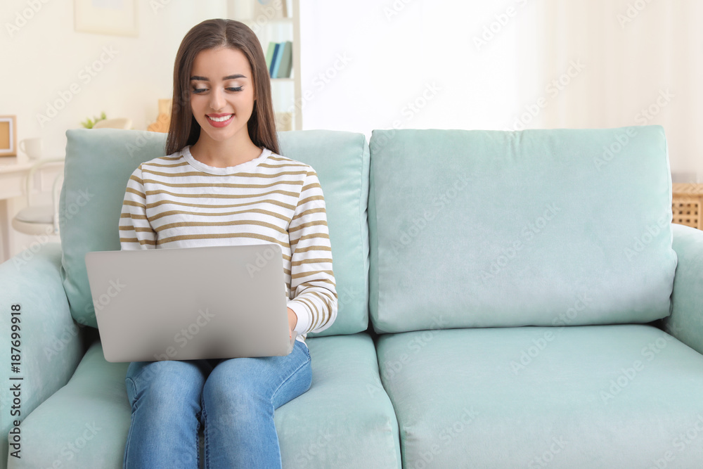 Young woman with modern laptop sitting on sofa at home Young woman with modern laptop sitting on sofa at home