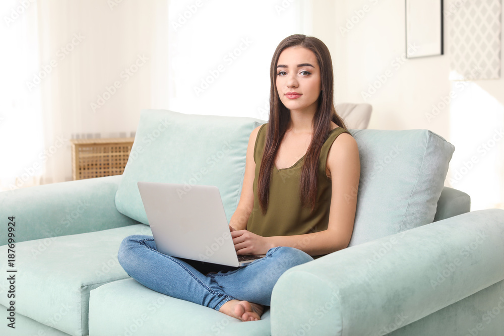 Young woman with modern laptop sitting on sofa at home Young woman with modern laptop sitting on sofa at home