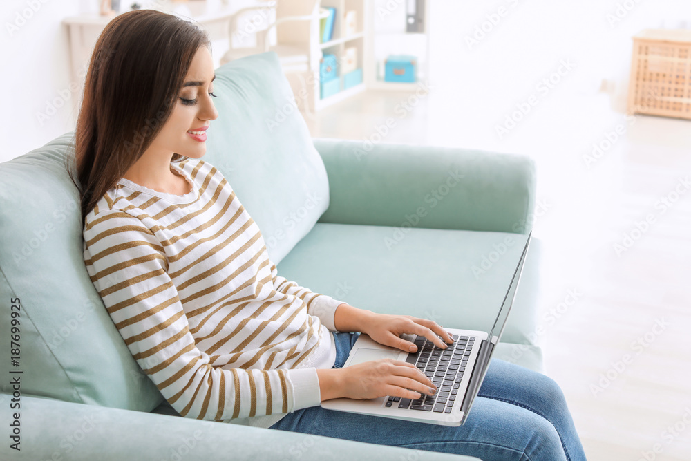 Young woman with modern laptop sitting on sofa at home Young woman with modern laptop sitting on sofa at home