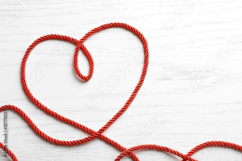 Heart made of red rope on white wooden background