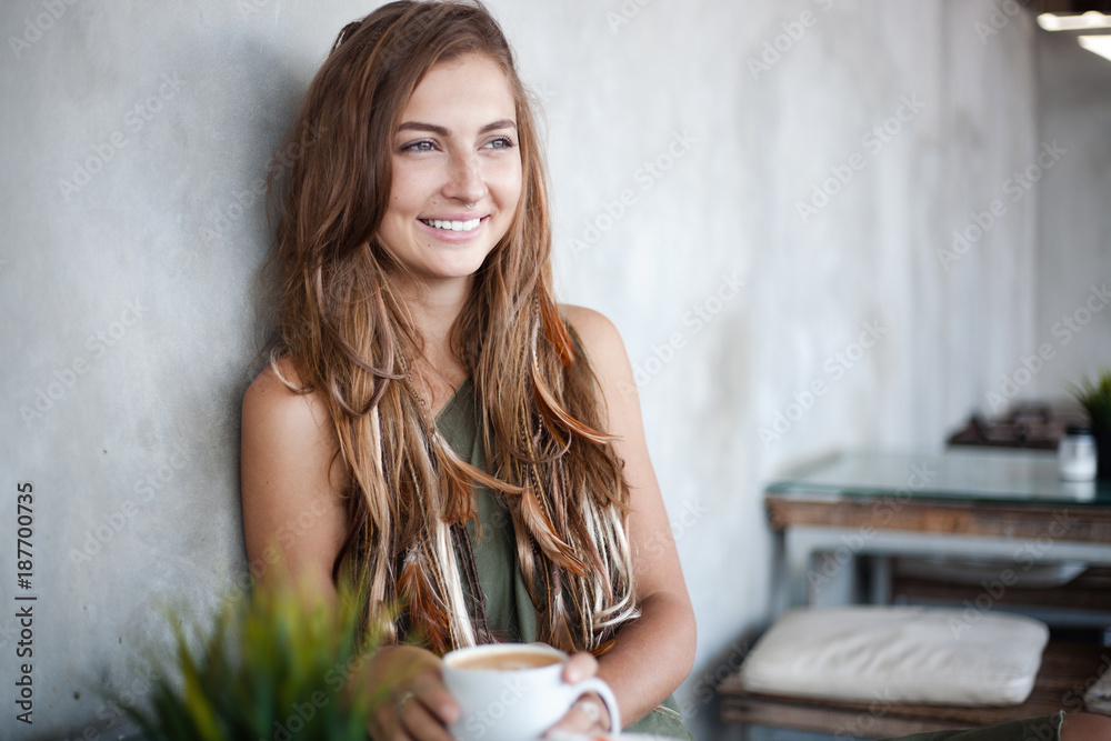 portrait of beautiful smiling girl is sitting in a cafe and holding cup of coffe portrait of beautiful smiling girl is sitting in a cafe and holding cup of coffe