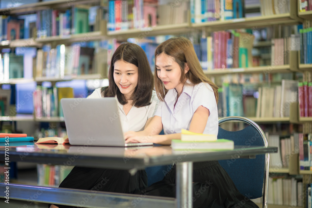 Two Asian students in uninifrom studying and doing research together in library at university. University student Two Asian students in uninifrom studying and doing research together in library at university. University student