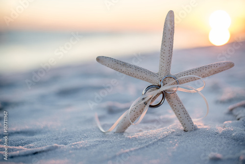 Wedding Rings tied to a Starfish Stuck in the Sand on the Beach with the Sunset in the Background