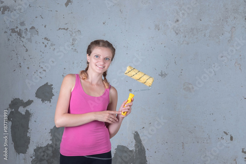 A beautiful girl is going to make repairs in the apartment and is standing with a roller for painting the walls