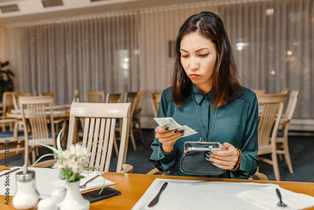 dissatisfied customer woman in the restaurant after dinner gets money out of her wallet to pay the bill, the concept of expensive prices in a cafe dissatisfied customer woman in the restaurant after dinner gets money out of her wallet to pay the bill, the concept of expensive prices in a cafe