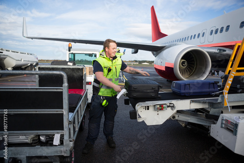 Fotografi Worker Arranging Luggage On Trailer Connected To Airplane