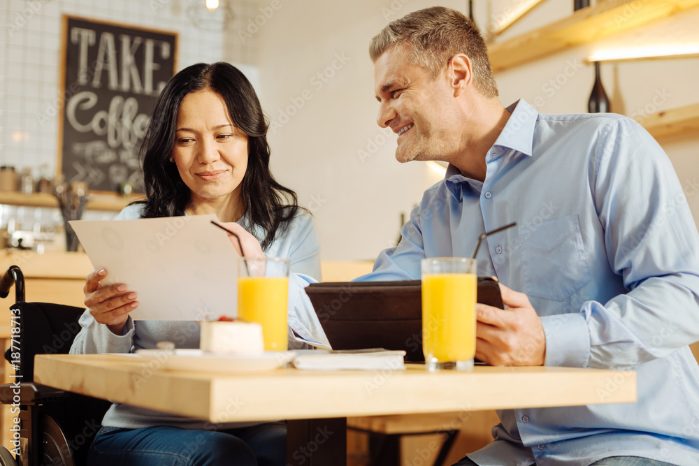 Team work. Beautiful joyful handicapped woman and a handsome cheerful blond man smiling and discussing work while sitting in cafe Team work. Beautiful joyful handicapped woman and a handsome cheerful blond man smiling and discussing work while sitting in cafe