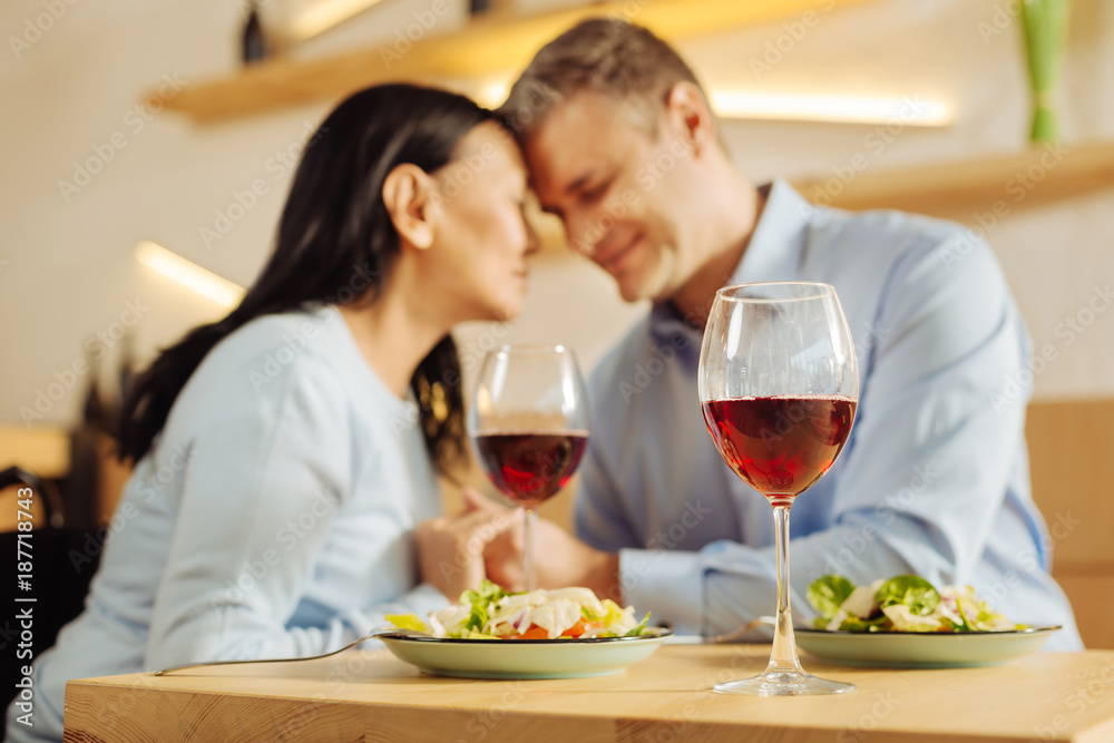 Wine. Beautiful happy disabled woman and an attractive smiling well-built man sitting in a cafe with eyes closed and holding hands and having dinner