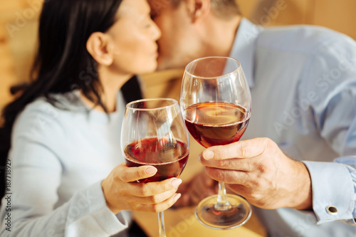 Red wine. Cheerful loving dark-haired woman and a content devoted well-built man sitting in a cafe and kissing and drinking wine