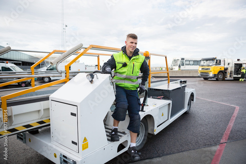 Fotografía Worker Disembarking Luggage Conveyor Truck On Airport Runway