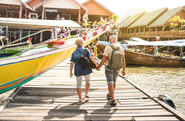Happy senior couple walking holding hand at Koh Panyi muslim floating village - Active elderly and travel lifestyle concept with retired mature people at Phang Nga bay Thailand - Warm day filter