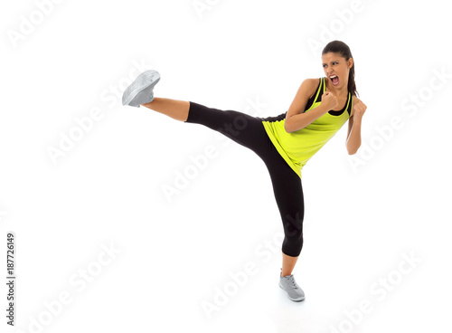 young attractive and furious hispanic sport woman in fight and kick boxing training workout throwing aggressive leg attack isolated