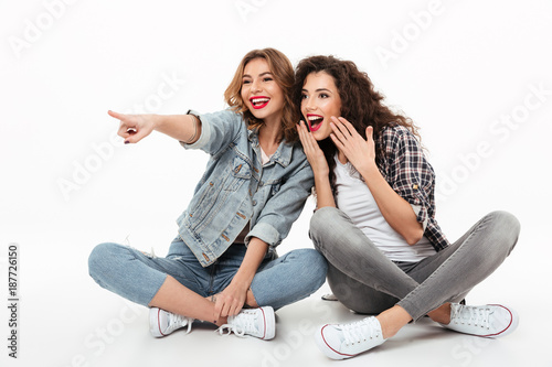 Two happy girls sitting on floor together and looking away