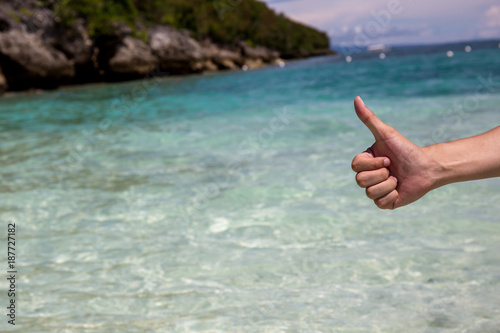 Close-up of thumbs up gesture in beach sea shore background.