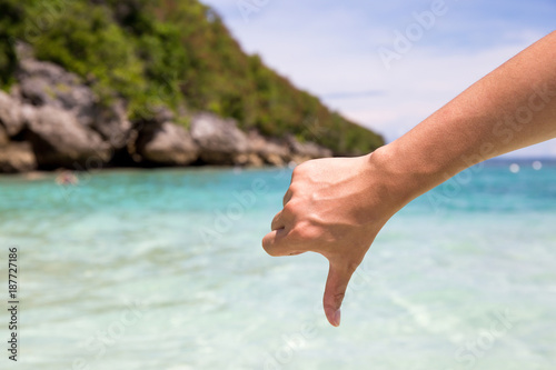 Close-up of thumbs down and dislike gesture in beach sea shore background. © twinsterphoto