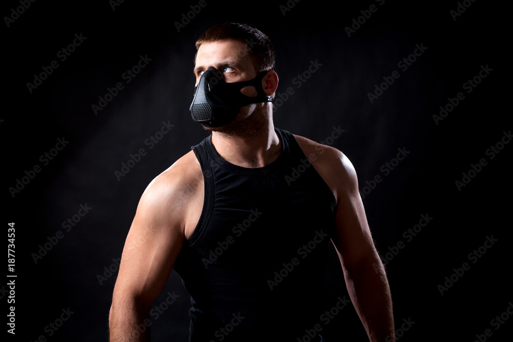 A dark-haired man athlete in a black training mask, a sports shirt pensively looking at a black isolated background