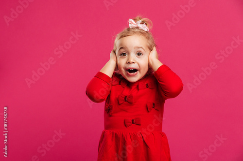 Shocked happy young girl in red dress holding her head