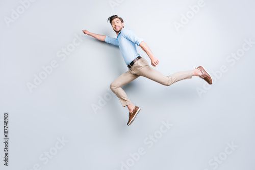 Happy, attractive, handsome, young man with bristle jumping in air showing superman pose looking at camera with beaming smile over grey background