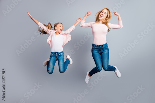 Cute, pretty, playful mother and daughter with open mouth jumping in the air over gray background, celebrating woman's day, yes, done, winners, victory, sisters screaming, shouting