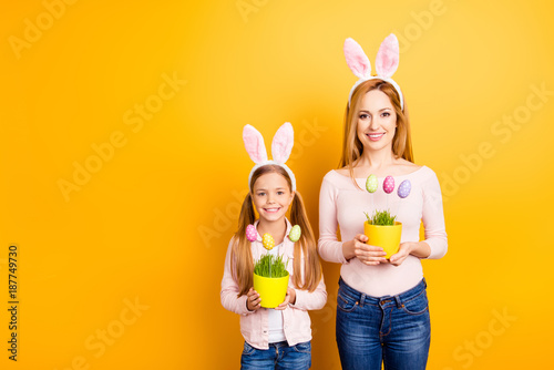 People gatherings family concept. Portrait of childish adorable sweet playful tender gentle mom and preteen girl holding two hand-crafted vases with dotted funny eggs on sticks isolated on background