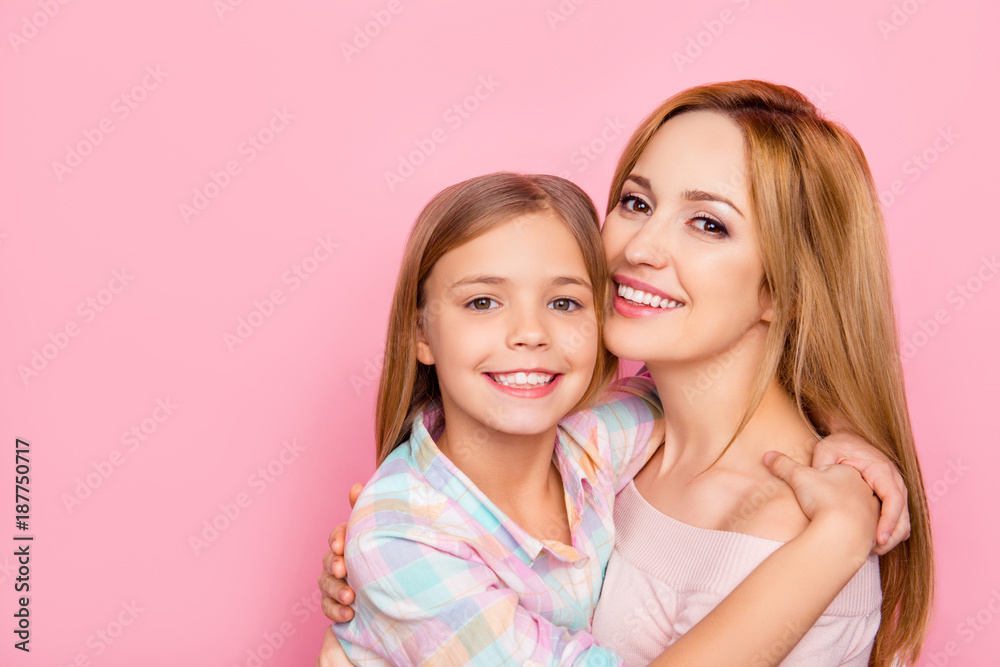 Close up portrait of pretty, charming mother and daughter with beaming smiles over pink background, bonding cheek to cheek, hugging, looking at camera, women's day