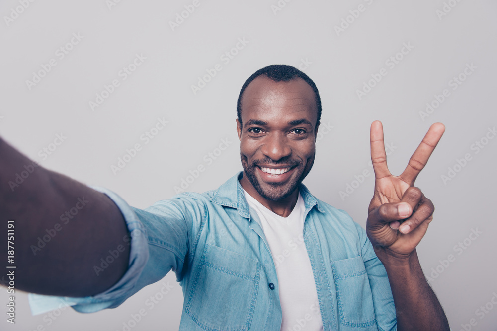 Close up portrait of glad excited cheerful handsome with beaming toothy smile foreigner demonstrating two sign and taking self portrait isolated on gray background