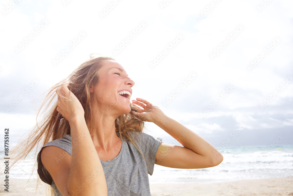 Beautiful young woman laughing at the beach with hand in hair