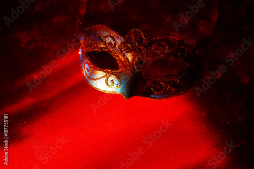 Image of elegant blue and gold venetian, mardi gras mask over red background. Magical glitter ovrlay.
