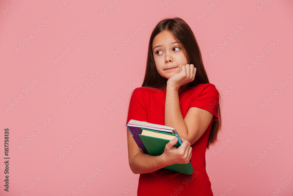Pensive girl pupil holding books and looking aside over pink Pensive girl pupil holding books and looking aside over pink