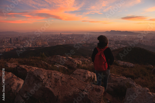 Girl watching beautiful sunset and city from mountain top