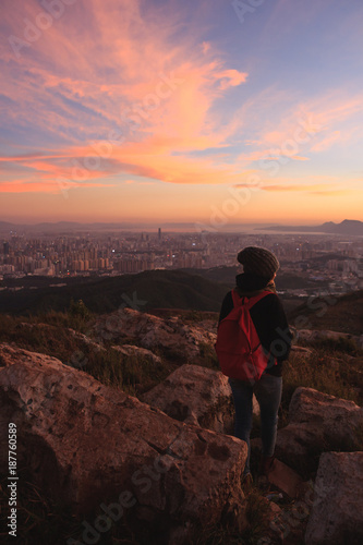 Girl watching beautiful sunset and city from mountain top