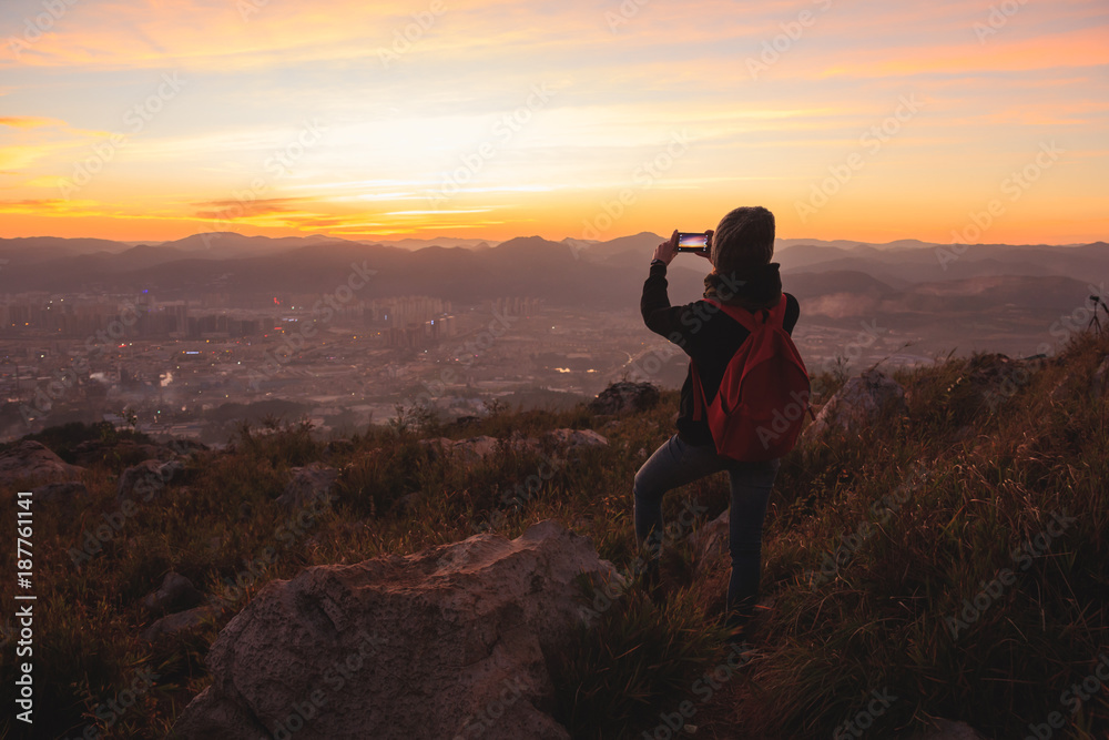 Girl taking pictures of beautiful sunset view with city and mountains