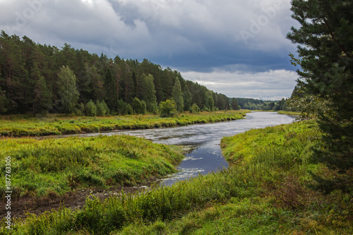 River flowing gently through woodland landscape, view before a thunderstorm. Location in Russia, Tverskaya oblast