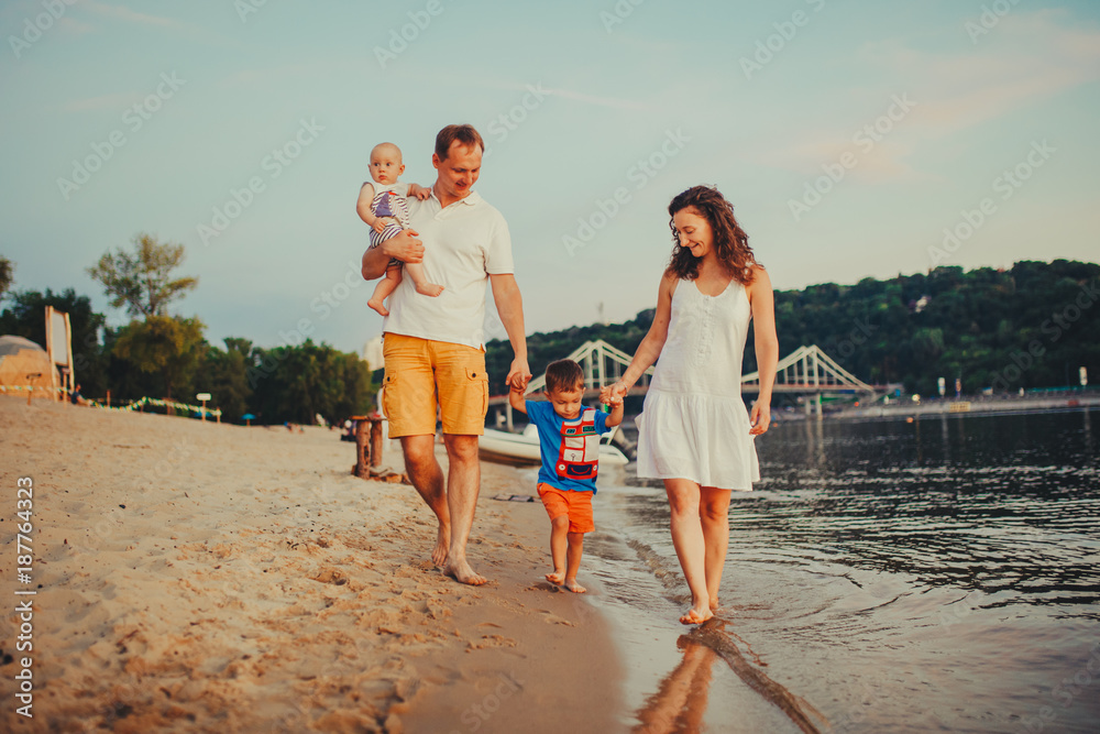 concept family beach vacation. Family of four people mom, dad and brothers children boys walking, want barefoot on the river bank by the hand at sunset in the summer