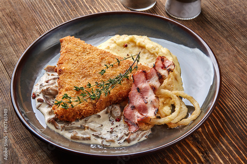 Chicken schnitzel with herb, mashed potatoes and mushrooms sauce on plate on wooden table background. Healthy food.