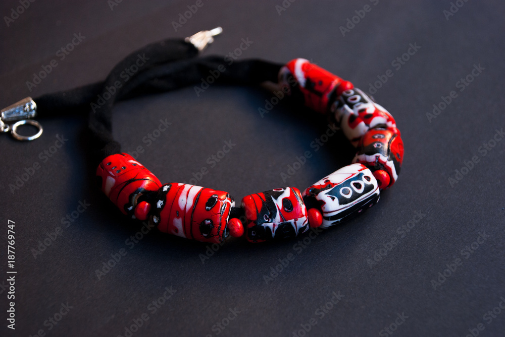 Fototapeta premium Handmade jewelry from polymer clay. Beautiful bright necklace on black background. Fashion foto. Bijouterie in macro. Black and red collar.