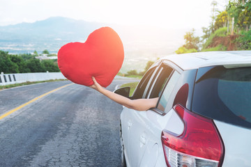 Relaxed happy traveler, Young beatiful asian gilr holding red heart and Reach out of the car at sunset and beautiful view with mountain road background