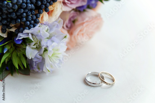 Beautiful wedding rings lie on a table against the background of a bouquet of flowers