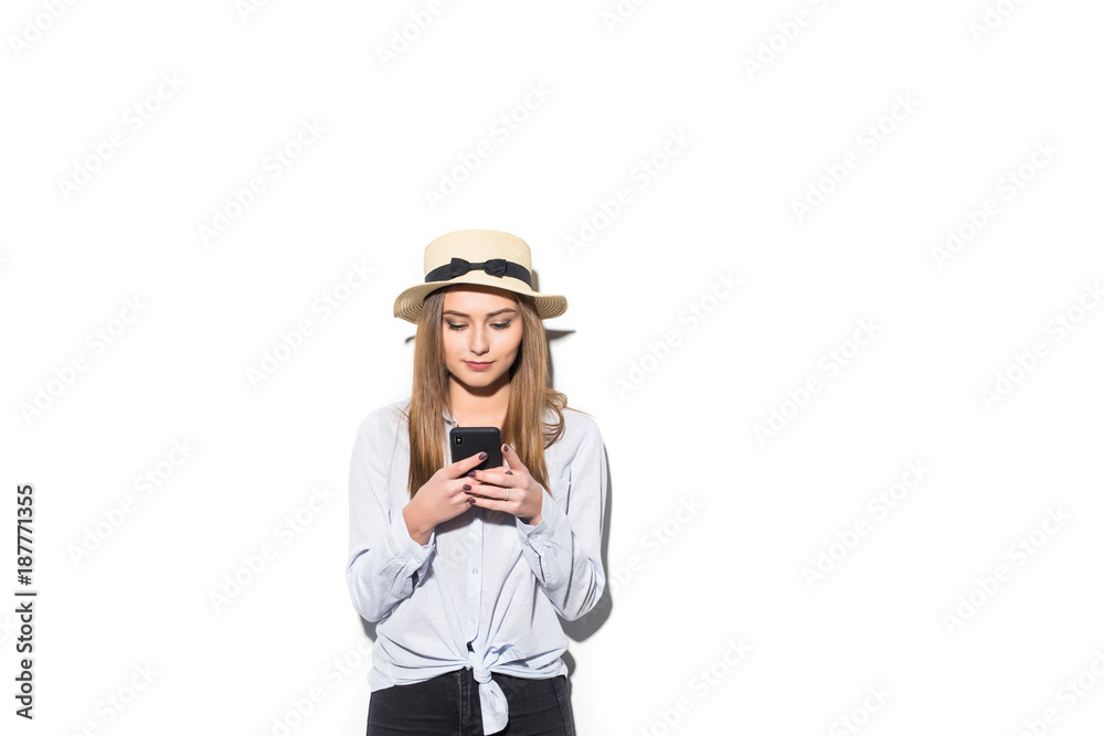 Cheerful girl in cap typing on smartphone on white background
