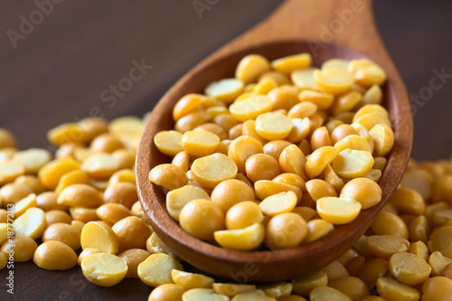 Raw yellow split peas in wooden spoon, photographed on dark wood with natural light (Selective Focus, Focus one third into the split peas in the spoon)
