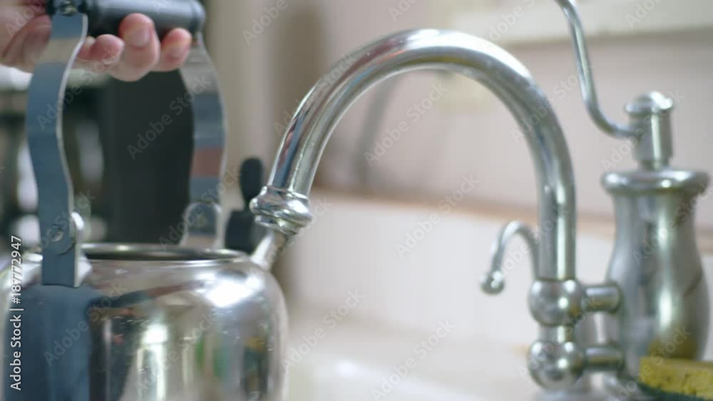 Young hispanic man fills stainless tea kettle at kitchen sink Young hispanic man fills stainless tea kettle at kitchen sink
