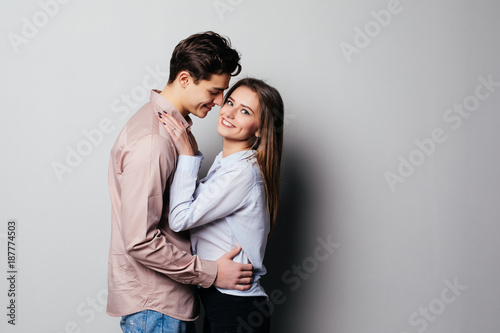 Vertical photo of two young cheerful people hugging each other against gray