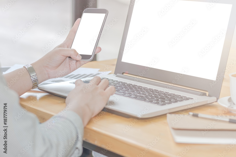 Close Up of woman hands using mobile phone and laptop computer with blank copy space screen for your advertising text message or content business at a coffee shop with a document. Close Up of woman hands using mobile phone and laptop computer with blank copy space screen for your advertising text message or content business at a coffee shop with a document.