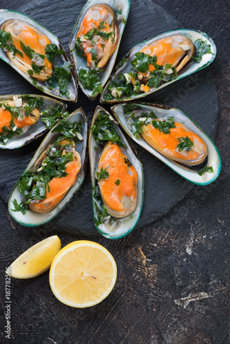Top view of boiled kiwi mussels with parsley and lemon on a stone slate, vertical shot, close-up
