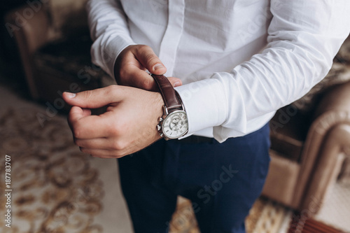 the groom in a white shirt adjusts his hand on his watch